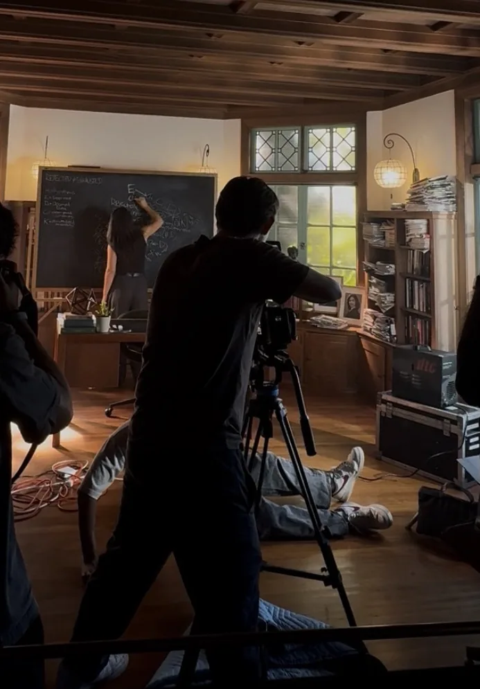 The camera operator filming the actress writing on the chalkboard