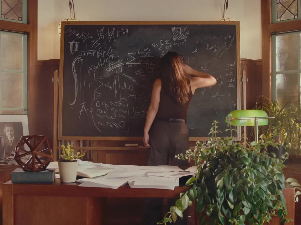 A researcher at a chalkboard full of equations in a sunlit wood-paneled study